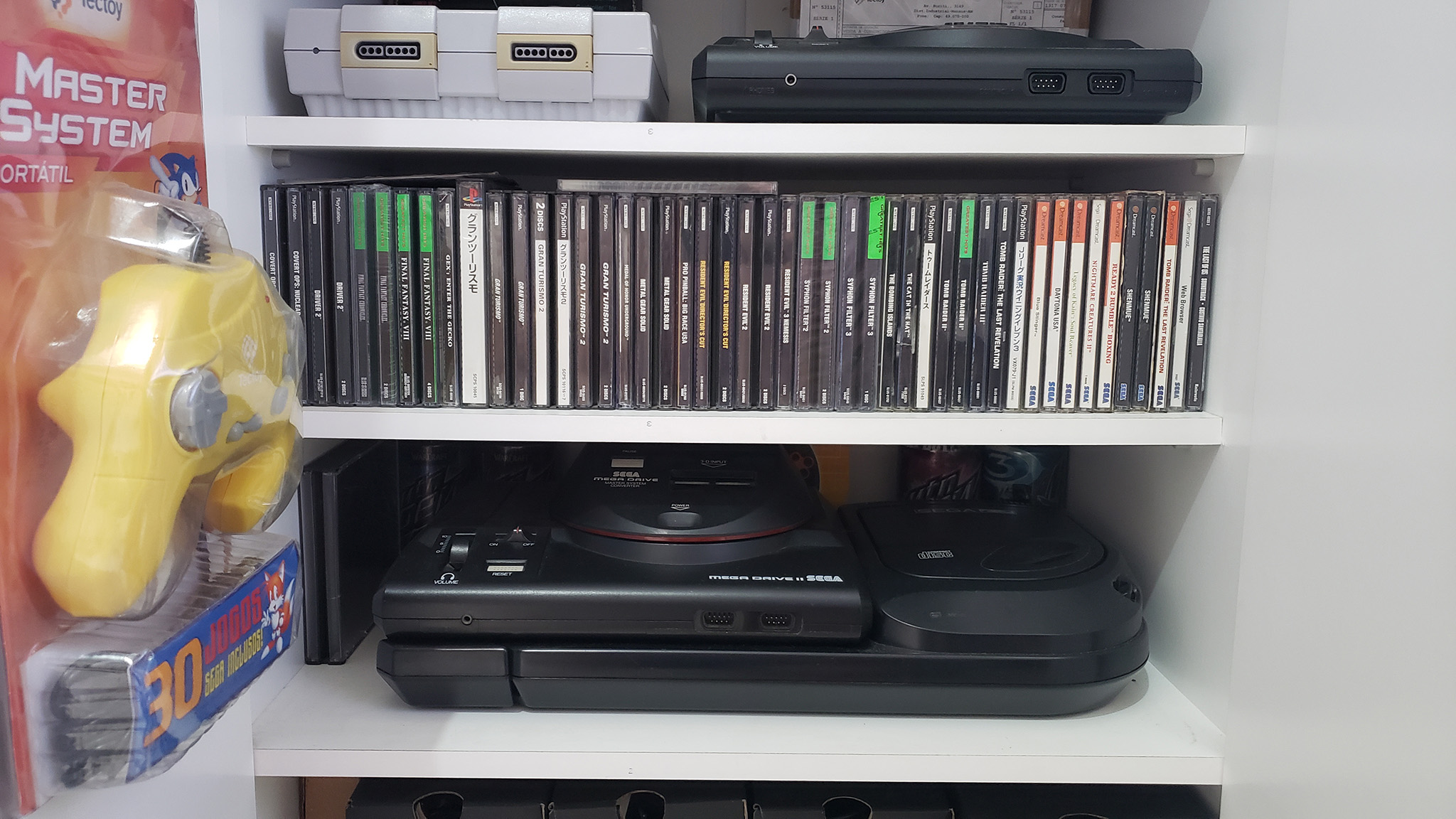 
  
    Minha coleção de PlayStation e Dreamcast. E na prateleira debaixo, um dos xodós: o quase 'Megazord' Mega Drive II com Sega CD e adaptador para Master System!
  
